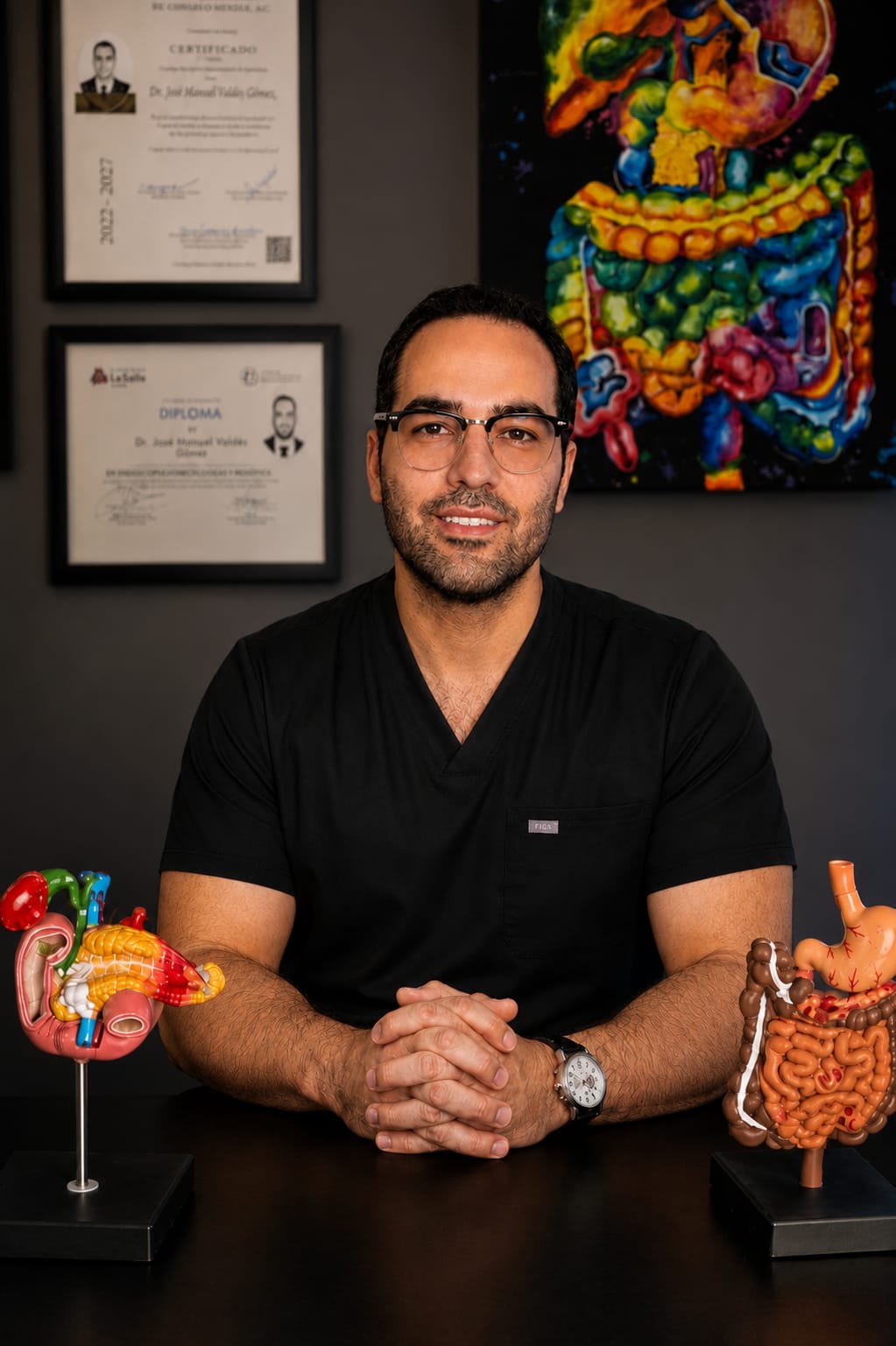 Dr. José Manuel Valdez Gómez, cirujano general en CDMX, en consultorio médico con modelos anatómicos digestivos.
